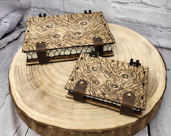 May include: Two wooden boxes with a carved design of a face with eyes and a mouth. The boxes are on a wooden surface.