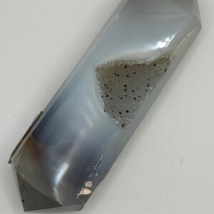 May include: A faceted, elongated crystal with a polished, translucent gray exterior. A cavity reveals a cluster of small, sparkling crystals. The crystal's shape is geometric, with multiple flat surfaces meeting at sharp angles.
