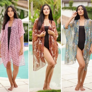 May include: Three women wearing different patterned sheer cover-ups over black swimsuits. The cover-ups are in pink, brown, and blue.