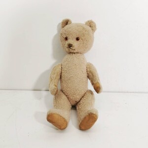 Puede incluir: Un oso de peluche vintage de color marrón claro, sentado. Tiene una nariz cosida, ojos marrones pequeños y patas de color marrón claro. Un juguete clásico.