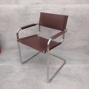 Könnte beinhalten: Moderner Stuhl aus braunem Leder mit verchromtem Gestell. Der Stuhl hat ein freitragendes Design mit rechteckiger Sitzfläche und Rückenlehne. Die Armlehnen sind ebenfalls mit braunem Leder bezogen. Ein stilvolles Möbelstück.
