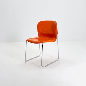 May include: An orange plastic chair with a curved back and seat. The chair has a chrome-colored metal frame. The chair is a modern design and is suitable for indoor use.