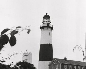 Puede incluir: Un faro blanco y negro con una torre de rayas blancas y negras se alza alto contra un cielo nublado. El faro está rodeado de vegetación verde.