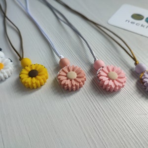 Peut inclure: Cinq colliers avec des breloques de fleurs colorées et des cordons de différentes couleurs. Les breloques sont blanches, jaunes, roses et violettes.