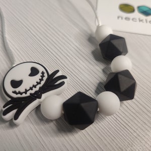 Könnte beinhalten: Eine schwarz-weiße Silikonkette mit einem Jack Skellington-Anhänger und geometrischen Perlen. Die Kette liegt auf einer weißen Oberfläche. necklactic