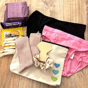 May include: A beige canvas pouch with embroidered hearts, a pink and black pair of underwear with the text "Bonds" on the waistband, a pair of pink socks, a hair scrunchie, and a diamond-shaped object.