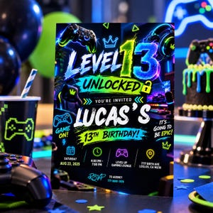 以下が含まれることがあります： 黒い背景にネオングリーンとブルーのゲームグラフィックが描かれた長方形の誕生日招待状。テキストには「Level 13 Unlocked」「Lucas's 13th Birthday」「2025年8月23日土曜日」「午後4時〜午後7時」「Level Up Gaming Lounge」「7777 Birth Ave, Loslos, CA 90210」「RSVP to Audrey 777-8880-7878」と記載されています。