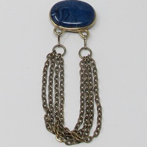 May include: Gold-tone necklace with a blue oval pendant and multiple chain tassels. The pendant has a marbled appearance. The necklace is displayed against a white background.