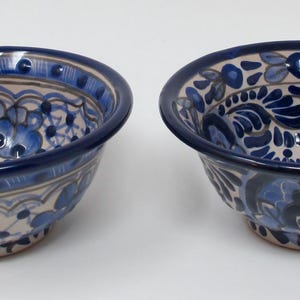 May include: Two ceramic bowls with intricate blue floral patterns on a cream background. The bowls have a dark blue rim and are likely handmade. These decorative bowls are suitable for serving or display.