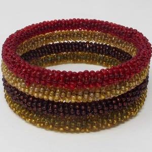 Puede incluir: Un brazalete de cuentas multicapa con cuatro filas de cuentas en tonos rojos, marrones y dorados.