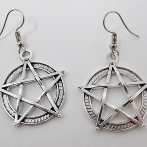 May include: Silver tone earrings with a pentagram design. The pentagram is surrounded by a circle with a textured edge.