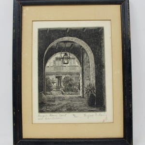 May include: Black framed print of a courtyard scene. The artwork, in black and white, depicts a series of archways leading to a building with a balcony. A hanging lantern is visible. The print is labeled "Bosque House Court, Old New Orleans."