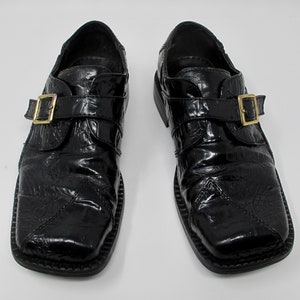 May include: A pair of black leather shoes with a buckle closure. The shoes have a textured, alligator-like pattern and a square toe.