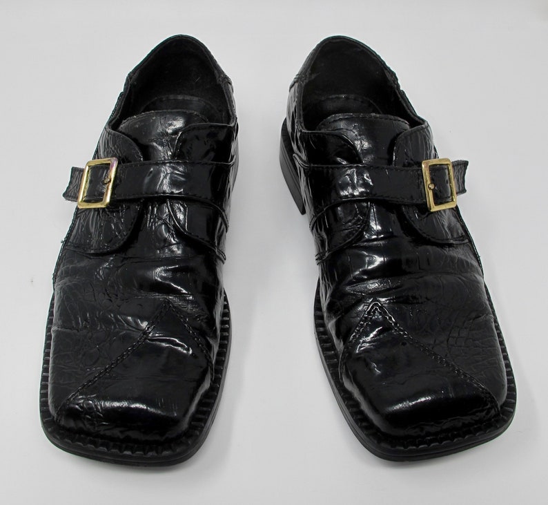 May include: A pair of black leather shoes with a buckle closure. The shoes have a textured, alligator-like pattern and a square toe.