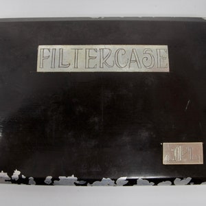 May include: A black cigarette case with a silver metal plate that reads "FILTERCASE" and a smaller silver plate with the number "2042".