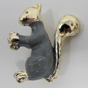 May include: A gray metal squirrel figurine with a gold-painted tail and head. The squirrel is standing on its hind legs with its front paws raised.