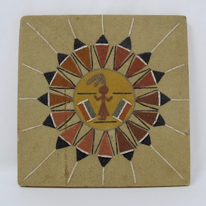 May include: A sand painting with a central figure in a yellow circle surrounded by a ring of brown, red, and black triangles. The figure is wearing a headdress and has outstretched arms.