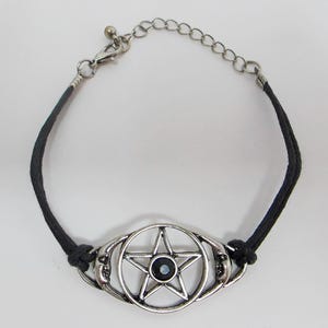 May include: Silver-toned bracelet featuring a pentagram design with a black center stone. The bracelet has a black cord band and a chain for adjustable sizing. The pentagram is set within a circular frame with crescent moon details.