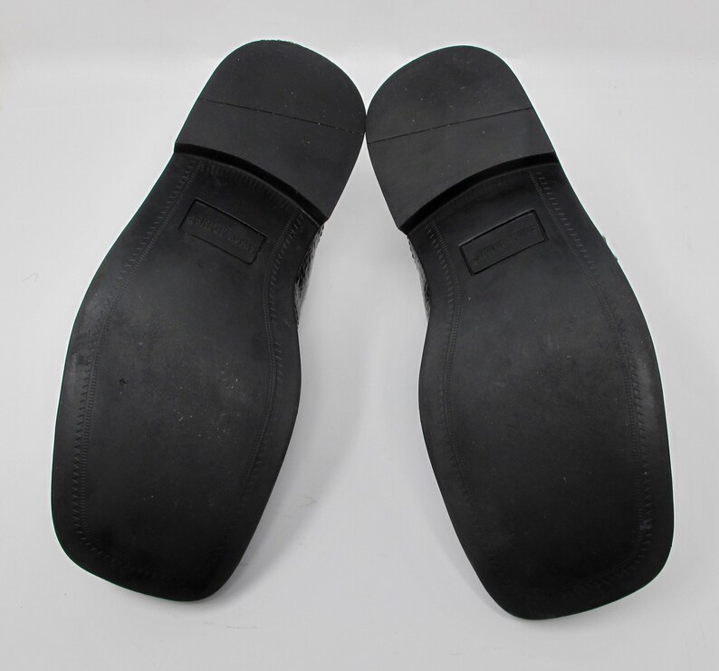May include: A pair of black leather dress shoes with a textured pattern on the upper. The shoes have a black rubber sole.