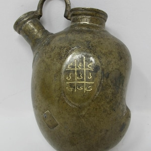 May include: A brass water jug with a handle and spout. The jug has a decorative inscription in gold lettering.