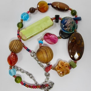 May include: A colorful necklace with wooden beads, ceramic beads, and glass beads. The necklace has a silver chain and a clasp.