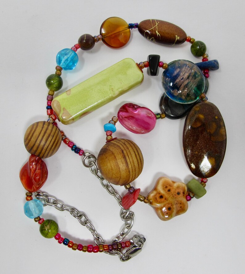 May include: A colorful necklace with wooden beads, ceramic beads, and glass beads. The necklace has a silver chain and a clasp.