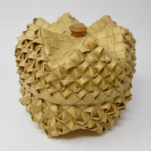 May include: A woven basket with a light brown color and a wooden lid. The basket is made of tightly woven strips of material, creating a textured surface.