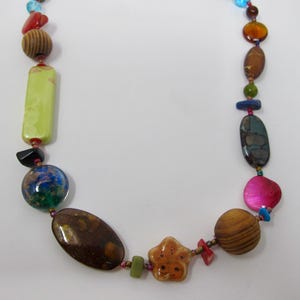 May include: A colorful necklace with various shapes and sizes of beads, including wood, stone, and glass. The beads are in shades of brown, green, blue, pink, and red.