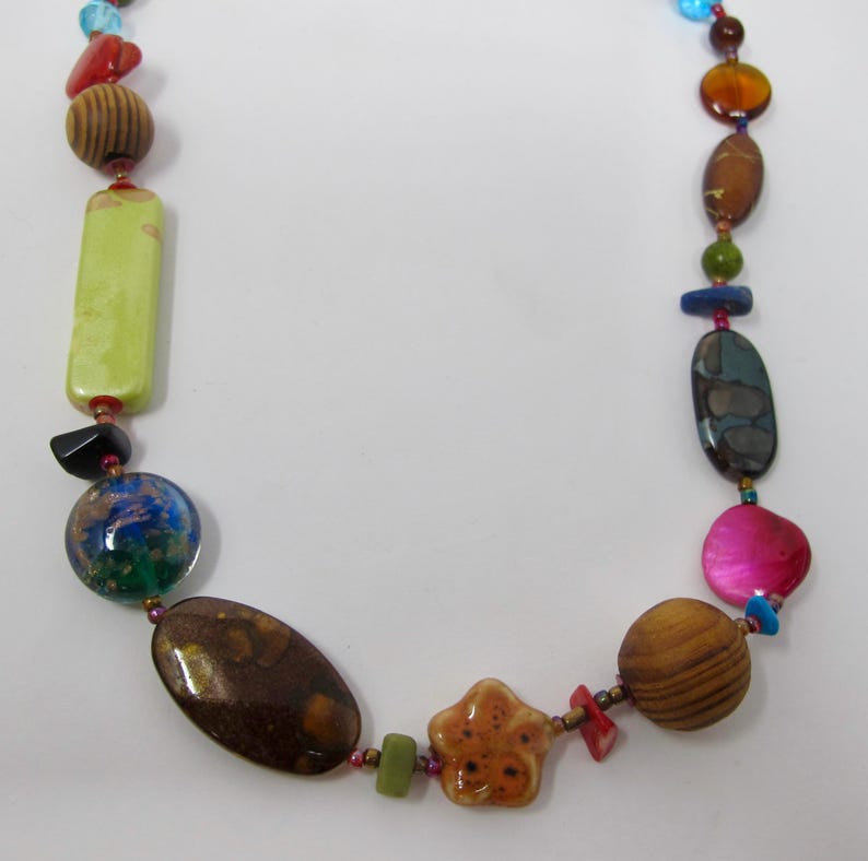May include: A colorful necklace with various shapes and sizes of beads, including wood, stone, and glass. The beads are in shades of brown, green, blue, pink, and red.