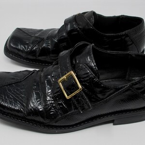 May include: A pair of black leather shoes with a crocodile-embossed pattern and a gold buckle. The shoes have a square toe and a low heel.