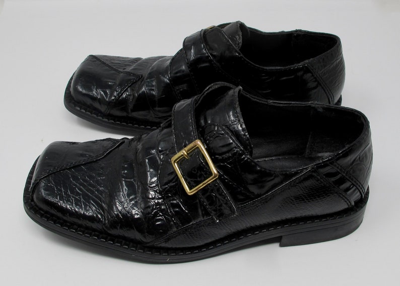 May include: A pair of black leather shoes with a crocodile-embossed pattern and a gold buckle. The shoes have a square toe and a low heel.