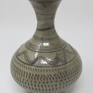 May include: A gray ceramic vase with a wide base and a narrow neck. The vase is decorated with a geometric pattern of brown lines and dots.