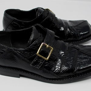 May include: A pair of black leather shoes with a crocodile-embossed pattern and a gold buckle. The shoes have a square toe and a low heel.