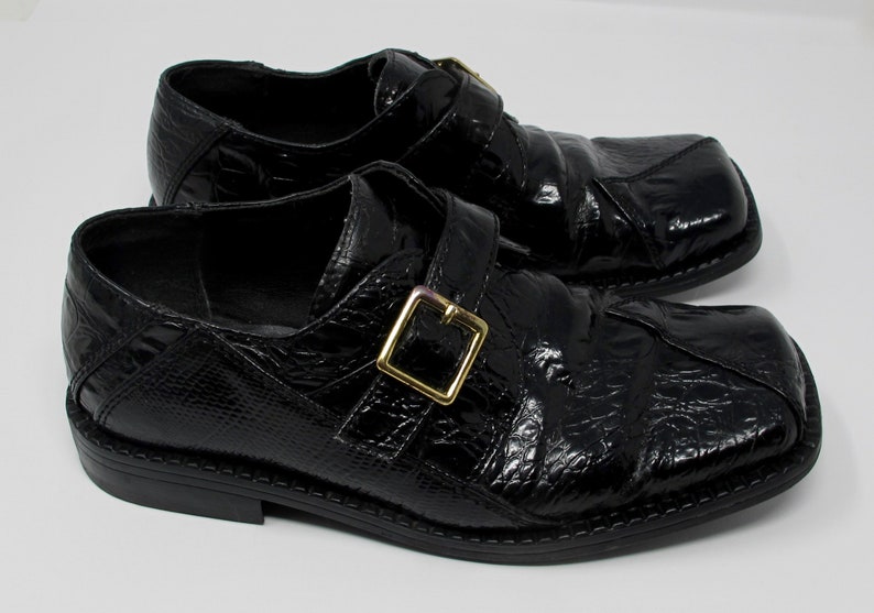 May include: A pair of black leather shoes with a crocodile-embossed pattern and a gold buckle. The shoes have a square toe and a low heel.