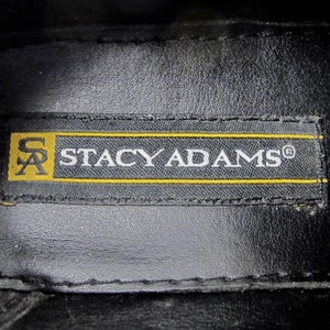 May include: Close-up of a black leather insole with a yellow label that reads "Stacy Adams&reg;" in white text.