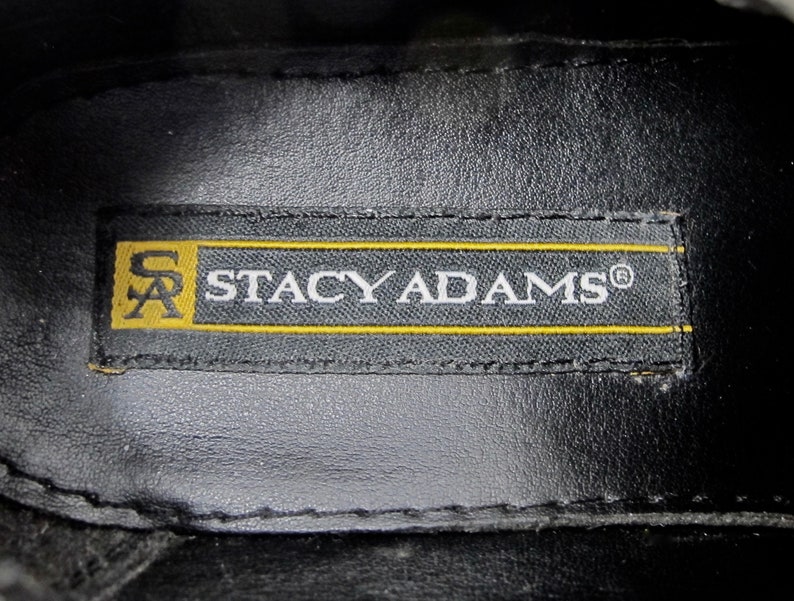 May include: Close-up of a black leather insole with a yellow label that reads "Stacy Adams&reg;" in white text.
