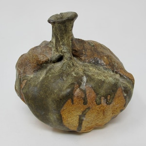 May include: A handcrafted ceramic vase with a bulbous body and a slender, cylindrical neck. The vase features a textured surface with earthy tones of brown, green, and tan, creating a rustic aesthetic. The vase is a unique decorative item.