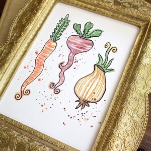 May include: Watercolor painting of a carrot, beet, and onion with green tops, framed in a gold ornate frame. The vegetables are depicted with whimsical details and watercolor splatters. The frame has a detailed floral pattern.