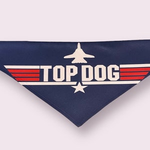 May include: A navy blue dog bandana with a white star and red stripes. The bandana features a white airplane and the text "TOP DOG".