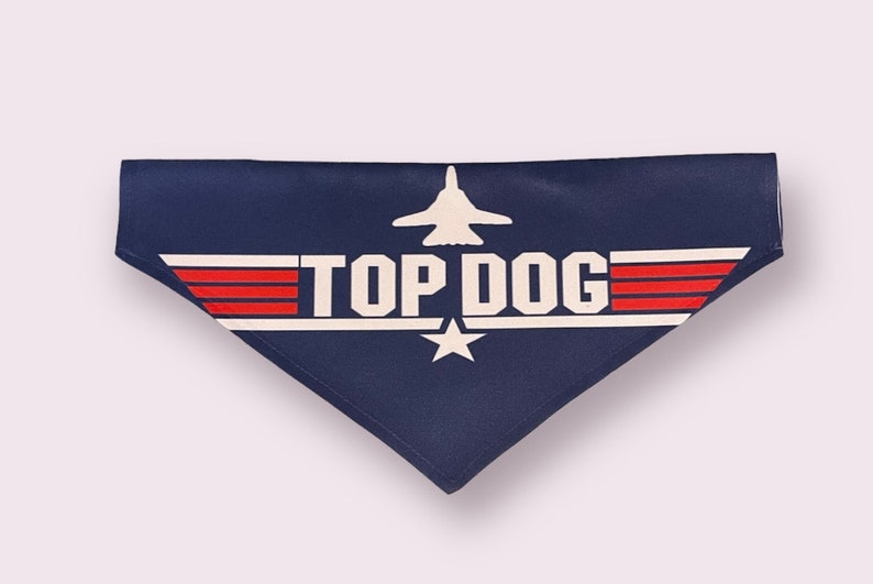 May include: A navy blue dog bandana with a white star and red stripes. The bandana features a white airplane and the text "TOP DOG".