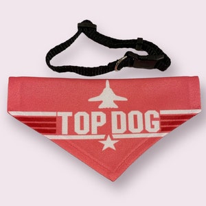 May include: A pink dog bandana with a white airplane and the text "TOP DOG" in white. The bandana has a black adjustable collar.