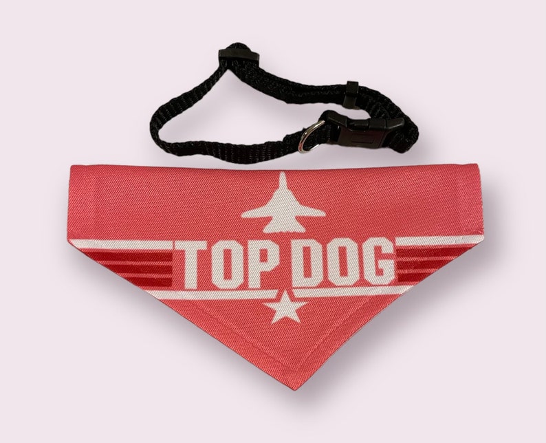 May include: A pink dog bandana with a white airplane and the text "TOP DOG" in white. The bandana has a black adjustable collar.
