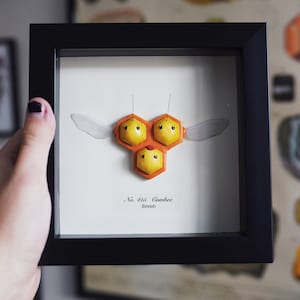 May include: A framed illustration of a yellow and orange Pokemon called Combee. The illustration is labeled "No. 415 Combee Sinnoh".
