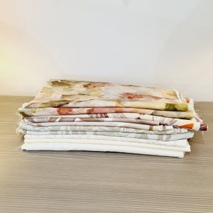May include: A stack of fabric squares in various shades of beige, brown, and pink with floral patterns. The fabric is soft and has a subtle sheen.