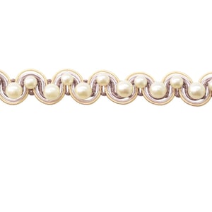 May include: A decorative trim with a repeating pattern of cream-coloured faux pearls set within a wavy design. The trim has a light gold and mauve colour scheme, suitable for embellishing craft projects.