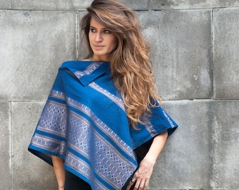 May include: A woman wearing a blue and silver patterned poncho with a long, wavy brown hair style.