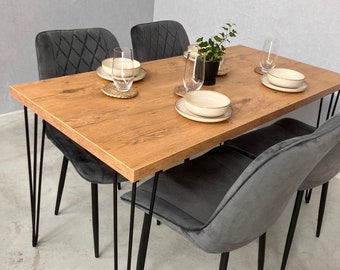 May include: A wooden dining table with black hairpin legs and four gray velvet chairs. The table is set with plates, glasses, and a small potted plant.