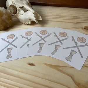 May include: Five white cards with a pentacle, two crossed swords, and a chalice in the center. The cards are arranged in a fan shape.