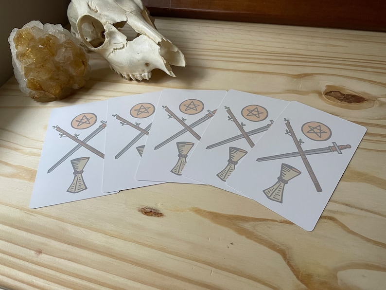 May include: Five white cards with a pentacle, two crossed swords, and a chalice in the center. The cards are arranged in a fan shape.