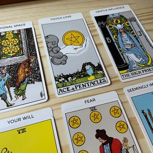 May include: Tarot card spread with ten cards, including the Ace of Pentacles, The High Priestess, and the Eight of Wands. The cards are laid out on a wooden surface. The cards have titles such as "Touch Love", "Emotional Space", "Gentle Influence", "Your Will", "Fear", and "Seemingly Impossible".